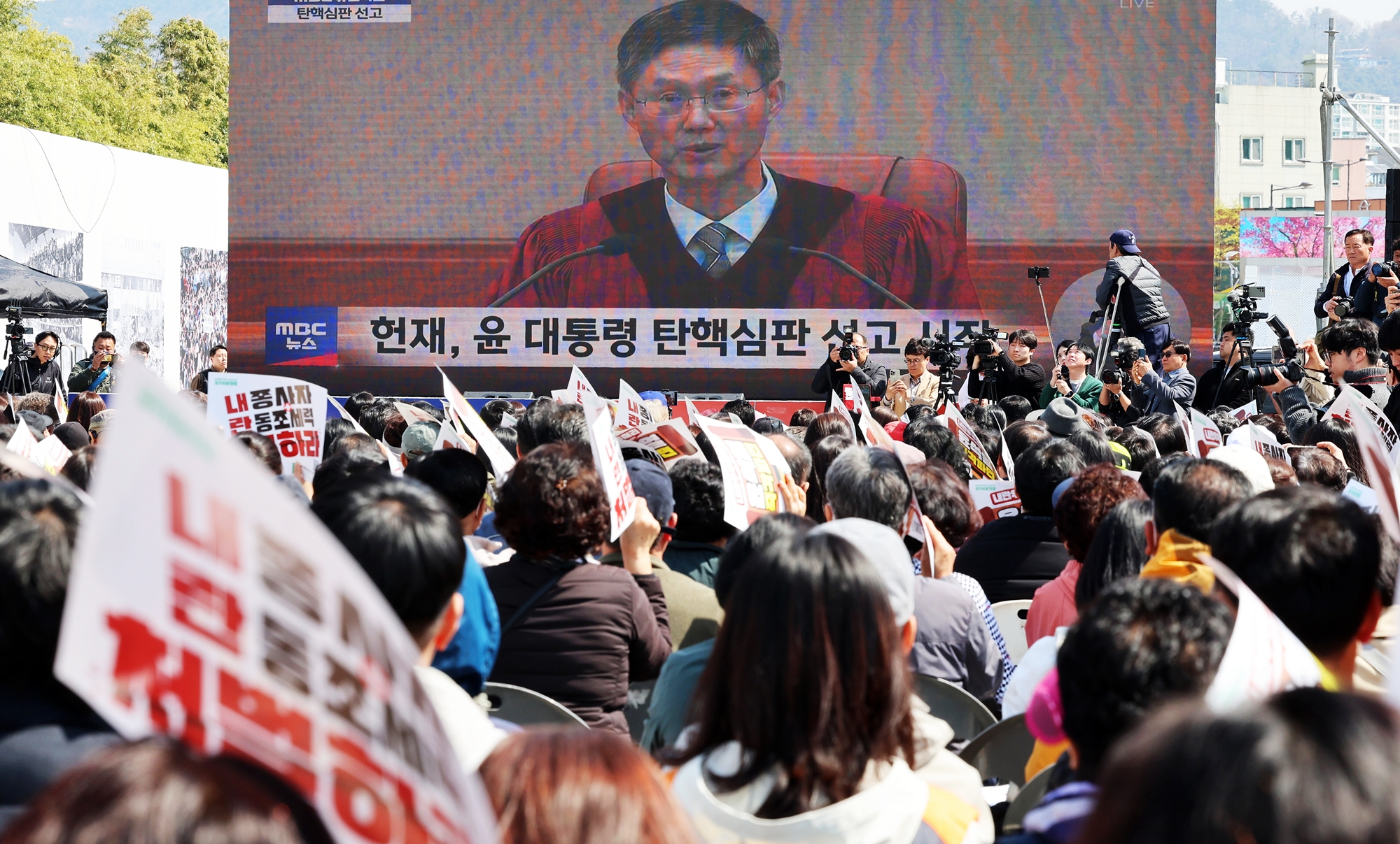 Конституционный суд Республики Корея 4 апреля единогласно утвердил импичмент президента Юн Сок Ёля. За импичмент выступили все восемь судей. Решение было вынесено через 122 дня после того, как 3 декабря прошлого года Юн Сок Ёль объявил военное положение в Корее, и спустя 111 дней после подачи прошения об импичменте 14 декабря. На фото горожане смотрят прямую трансляцию заседания Конституционного суда по делу об импичменте на Площади Движения за демократию 18 мая в Кванджу. / Фото: Рёнхап 