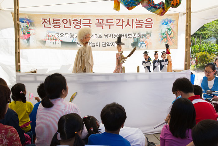 Children enjoy a <i>kkokdu</i>wooden puppet performance about the importance of having a good harvest, at the National Folk Museum of Korea.