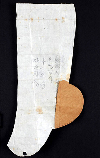 A pattern for a pair of <i>beoseon</i> socks is donated by Yi Seung-hui. Her mother made the pattern for her by hand, with a moveable paper piece in the heel, and wrote her wishes and hopes on the side of the pattern.